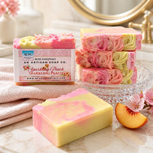 A bar of handmade cold process goat's milk soap with pink and yellow layers, decorated with a floral design, next to a vase with peach flowers.